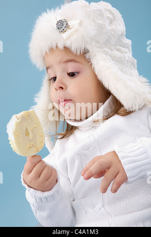 Petite fille en blanc le furry hat en regardant la glace dans ses mains Banque D'Images