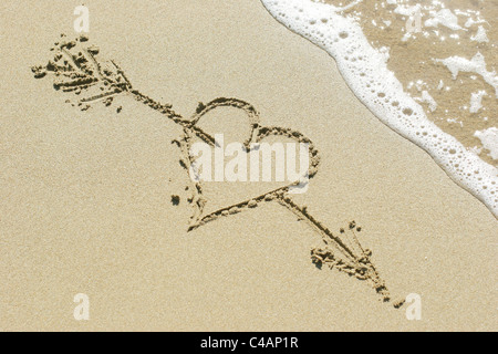 Cœur percé par la flèche de Cupidon dessiné dans le sable Banque D'Images