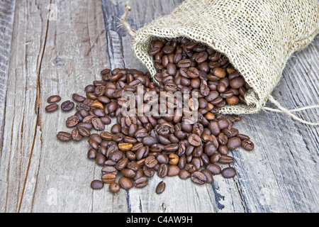 Grains de café dans un sac de jute sur une table en bois Banque D'Images