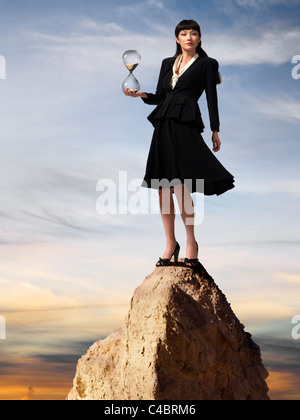 Asian business woman standing on hourglass mountaintop au coucher du soleil Banque D'Images