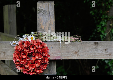 Une couronne de roses rouges artificielles et fatigué bande d'ox-eye tribunes placées sur une clôture en bois ressemblant à une croix. Banque D'Images