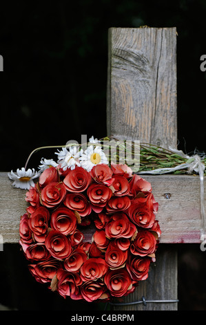 Une couronne de roses rouges artificielles et fatigué bande d'ox-eye tribunes placées sur une clôture en bois ressemblant à une croix. Banque D'Images