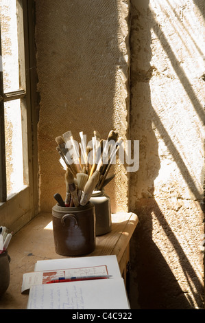 Les pinceaux en pots de terre cuite baigné de soleil sur une fenêtre dans un intérieur aux murs en pierre Banque D'Images