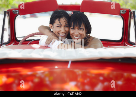 Jeune brunette adultes femmes double driving convertible voiture rouge et à la recherche sur les épaules. Vue arrière, de forme horizontale, copy space Banque D'Images