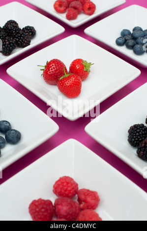 Fraises, framboises, bleuets et mûres dans des plats carrés sur fond rose Banque D'Images