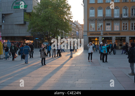 Les gens qui marchent le long de la zone piétonne qui mène au centre-ville, La Place Marienplatz, à la fin de soir lumière à Munich, Allemagne. Banque D'Images