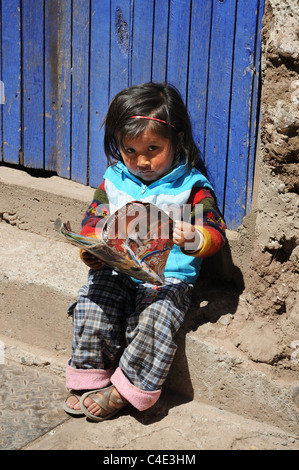 Une petite fille péruvienne peu la lecture d'un magazine dans une rue secondaire de Cusco Banque D'Images