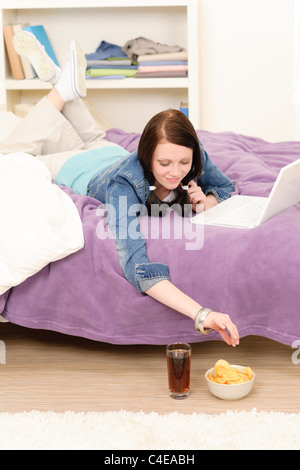 Jeune étudiante fille avec ordinateur portable ayant snack dans appartement d'étudiant Banque D'Images