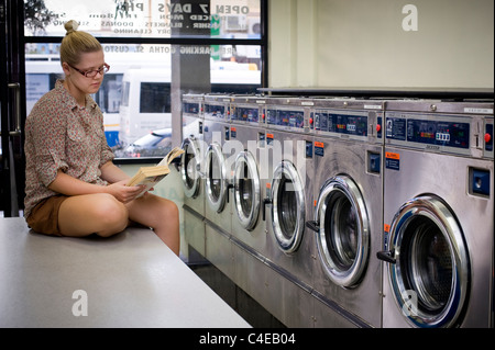 Young Woman Reading at laundromat Banque D'Images