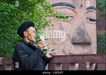 L'homme de boire du thé par les 71 mètres de Grand Bouddha de Leshan, le plus grand Bouddha Sculpté en pierre de droit dans le monde. Le Sichuan, Chine Banque D'Images