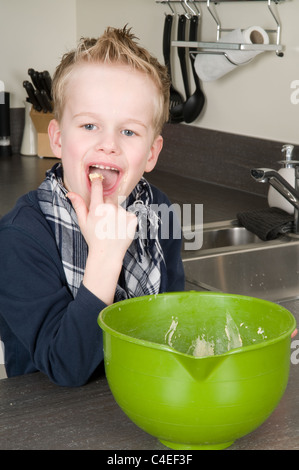 Boy eating la pâte qui est laissé derrière dans le bol. Banque D'Images