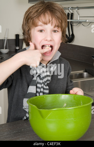 Boy eating la pâte qui est laissé derrière dans le bol. Banque D'Images