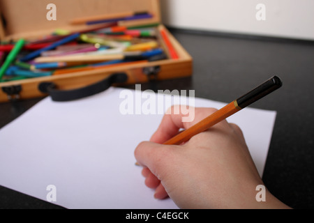 Une main tenant un crayon prêt à tirer, croquis et couleur sur un morceau de papier blanc ordinaire avec des couleurs à l'arrière-plan Banque D'Images