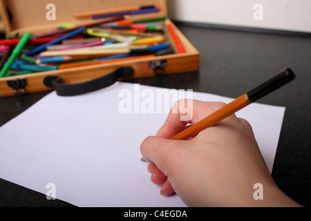 Une main tenant un crayon prêt à tirer, croquis et couleur sur un morceau de papier blanc ordinaire avec des couleurs à l'arrière-plan Banque D'Images