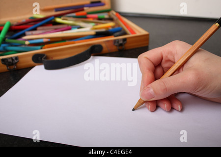 Une main tenant un crayon prêt à tirer, croquis et couleur sur un morceau de papier blanc ordinaire avec des couleurs à l'arrière-plan Banque D'Images