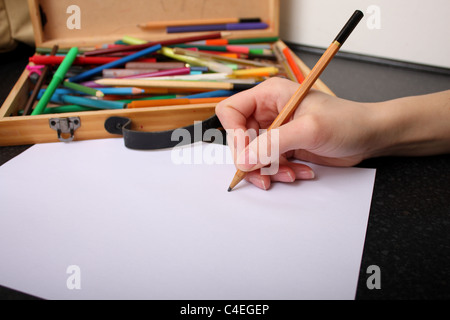 Une main tenant un crayon prêt à tirer, croquis et couleur sur un morceau de papier blanc ordinaire avec des couleurs à l'arrière-plan Banque D'Images