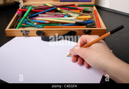 Une main tenant un crayon prêt à tirer, croquis et couleur sur un morceau de papier blanc ordinaire avec des couleurs à l'arrière-plan Banque D'Images