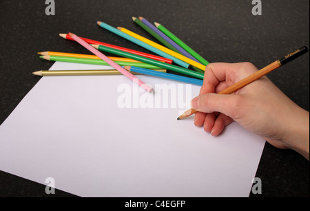 Une main tenant un crayon prêt à tirer, croquis et couleur sur un morceau de papier blanc ordinaire avec des couleurs à l'arrière-plan Banque D'Images