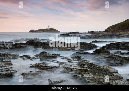 Les vagues déferlent sur les rochers de Godrevy Point au coucher du soleil, en regardant vers le phare de Godrevy, Cornwall, Angleterre. Banque D'Images