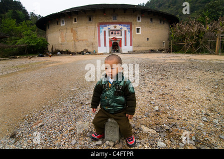 Un garçon Hakka, debout devant un grand bâtiment à Fujian Tulou. Banque D'Images