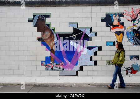 Une fille passe devant l'illustration de l'album de Pink Floyd le mur peint sur le mur de Berlin à l'East Side Gallery Banque D'Images