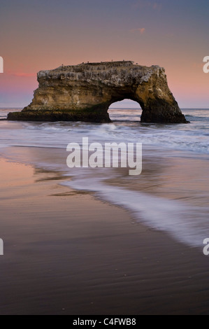 Arch Rock et des vagues sur la plage de sable dans la lumière du soir, Santa Cruz, Californie Banque D'Images