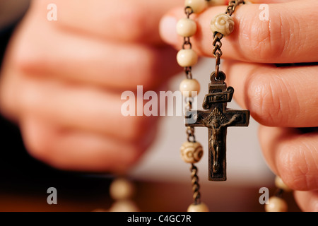 Femme (seulement close-up de mains pour être vu) avec l'envoi d'un rosaire prière à Dieu, le paramètre sombre suggère qu'elle est triste ou seule Banque D'Images