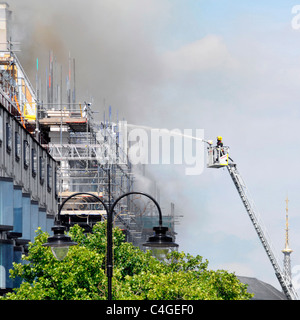 Pompier sur la plate-forme d'accès pulvérisant de l'eau sur le feu de toit à la maison Marconi reconstruction chantier de construction le Strand Londres Angleterre Royaume-Uni Banque D'Images