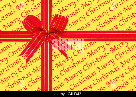Photo d'un cadeau enveloppé dans joyeux noël papier avec un ruban rouge et or attachés en un arc. Banque D'Images