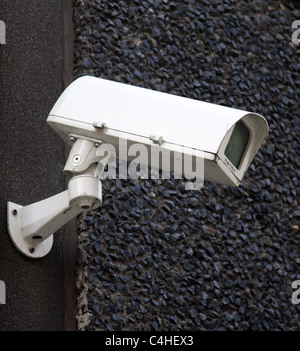 Caméra CCTV blanc sur le côté d'un mur en pointillés de galets gris Banque D'Images