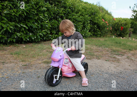 Enfant jouant sur un scooter jouet rose. Banque D'Images