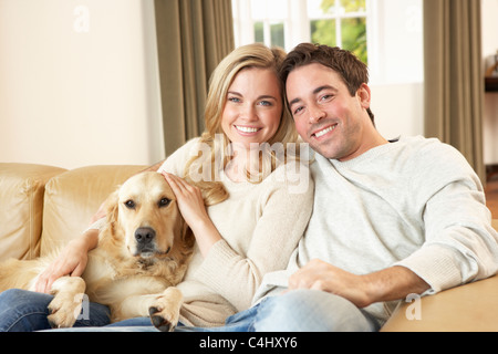 Jeune couple heureux avec chien assis sur le canapé Banque D'Images