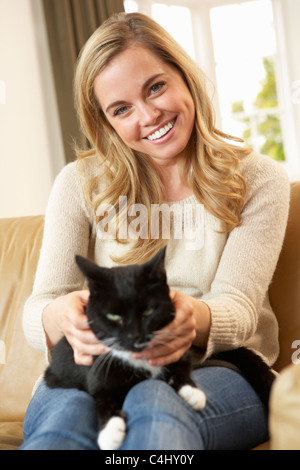 Happy young woman with cat sitting on sofa Banque D'Images