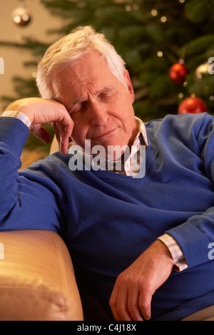 Fatigué Senior Man Relaxing in front of Christmas Tree Banque D'Images