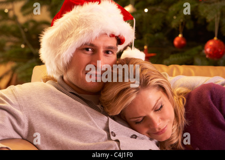 Fatigué Couple Relaxing in front of Christmas Tree Banque D'Images