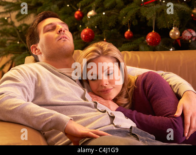 Fatigué Couple Relaxing in front of Christmas Tree Banque D'Images