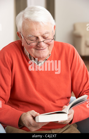 Senior Man Relaxing in Chair At Home Reading Book Banque D'Images