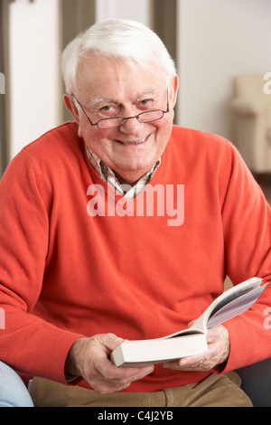 Senior Man Relaxing in Chair At Home Reading Book Banque D'Images