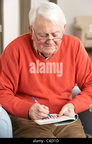 Senior Man Relaxing in Chair At Home remplissant Crossword Banque D'Images
