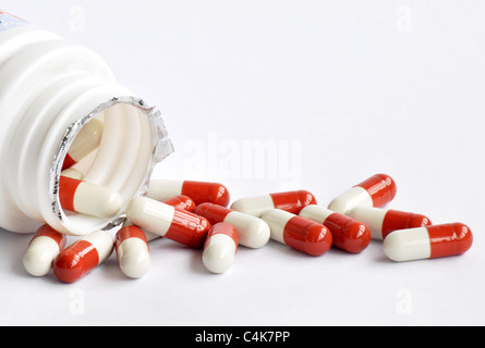 Vue rapprochée de la médecine rouge et blanc capsules spilling out d'une bouteille sur un fond blanc Banque D'Images