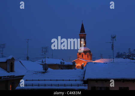 Vue de nuit sur les toits enneigés et église illuminée Madonna Moretta à Alba, dans le nord de l'Italie. Banque D'Images