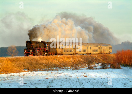 Soleil du soir prendre le loco de vapeur et des voitures qui est élevée sur une banque au-dessus de champs couverts de neige. Banque D'Images