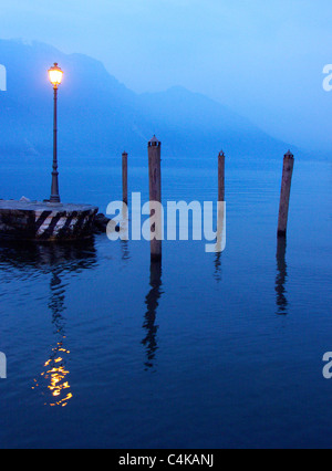 Soirée shot of landing stage avec lampe de rue sur le lac de Garde en Italie avec les montagnes couvertes de brume Banque D'Images