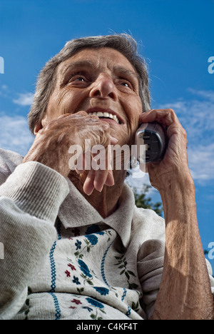 Une vieille femme, Senior citizen discussions sur un téléphone sans fil moderne, sur une journée ensoleillée. Banque D'Images