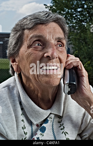 Une vieille femme senior sourit tout en parlant sur un téléphone sans fil. Banque D'Images