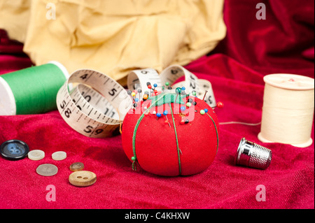 Une table de couture avec boutons, pin cushion, ruban à mesurer et virole. Banque D'Images