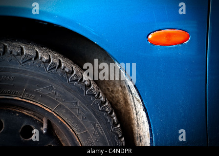 Le quart avant bleu-bord d'une voiture sale et rayé avec un quart du pneu montrant et réflecteur orange. Banque D'Images