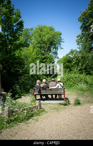 Quatre personnes assis sur un banc en Nunhead Cemetery à la recherche à travers des arbres à la Cathédrale St Paul. Banque D'Images