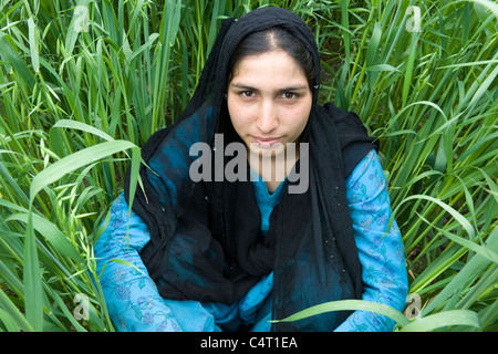 Cachemire femme assise dans l'herbe près de champs Manasbal Lake, dans l'état de Jammu-et-Cachemire, l'Inde Banque D'Images