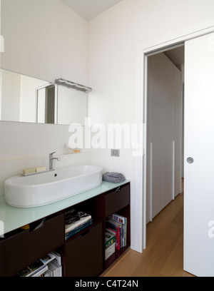 Salle de bains moderne avec sol en bois et lavabo blanc, porte coulissante. Banque D'Images